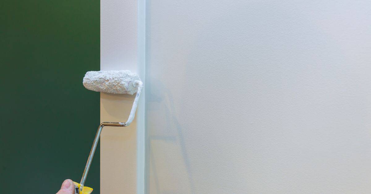 Paint roller applying white paint to outside wall corner
