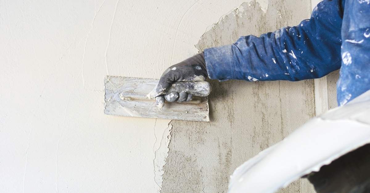 Gloved hand applying plaster with trowel on wall surface