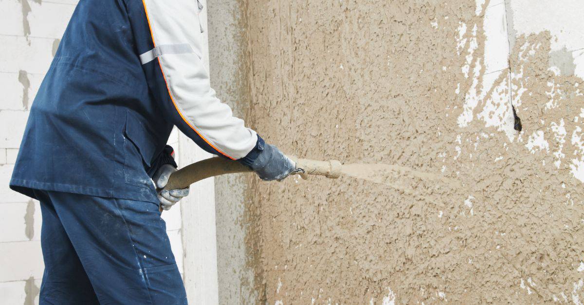 Worker spraying textured stucco onto wall surface