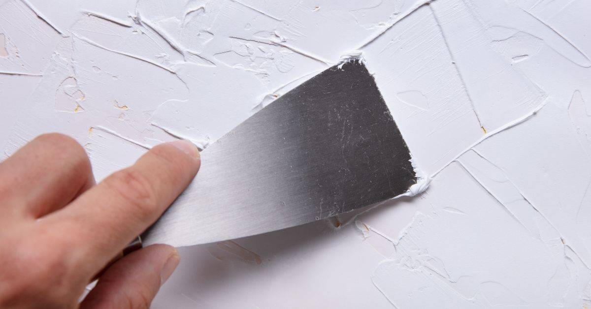 Hand applying white plaster with a metal putty knife