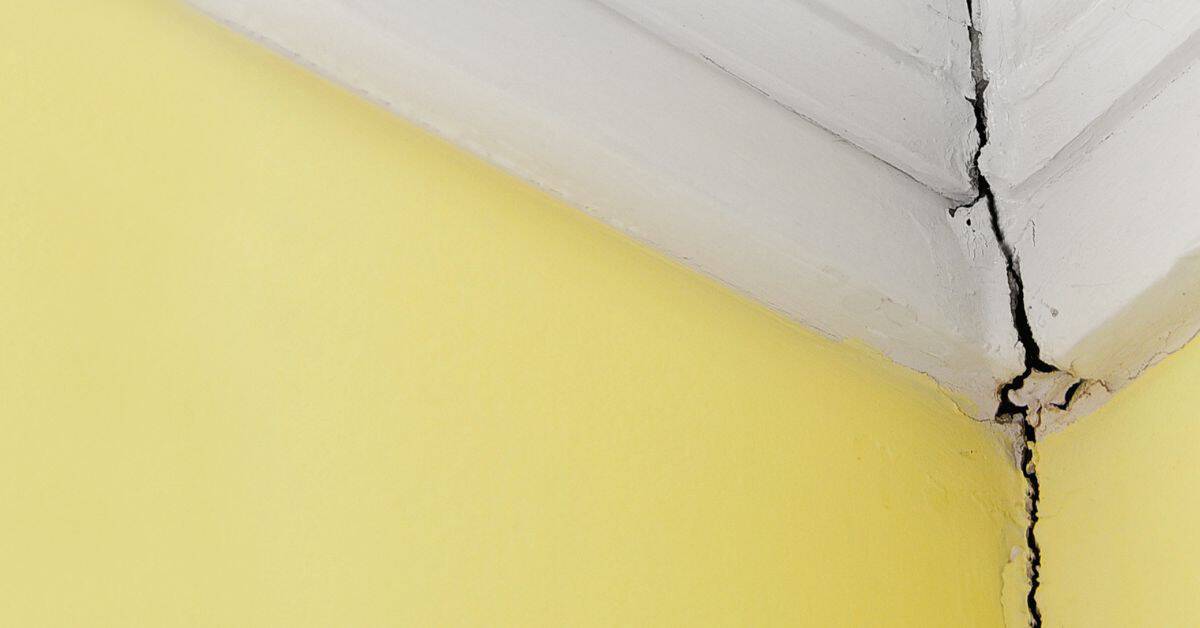 Cracked corner of white plaster wall above yellow painted wall