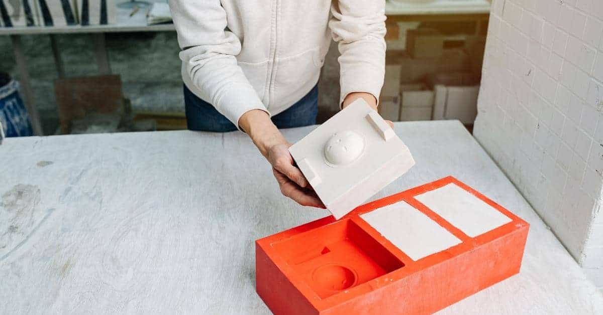 Person holding white plaster mold over red mold base on table