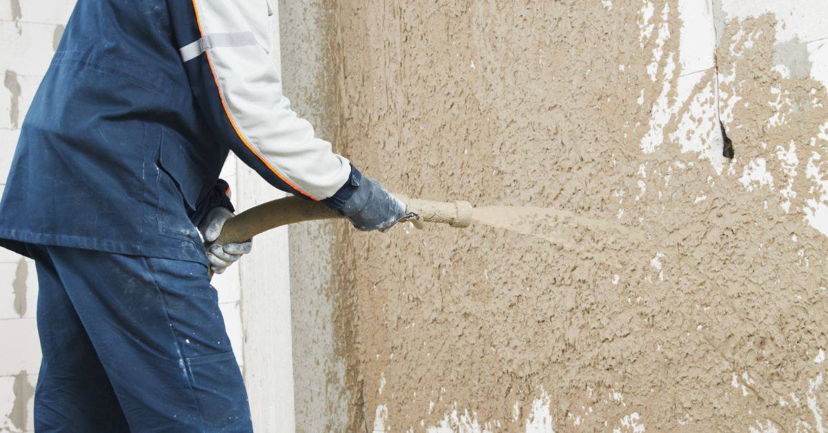 Worker spraying wet plaster onto wall