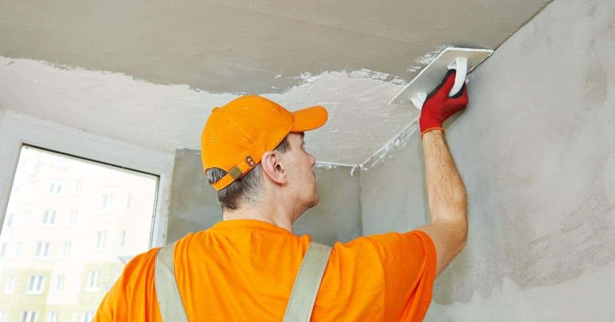 Worker applying plaster on ceiling with trowel wearing orange