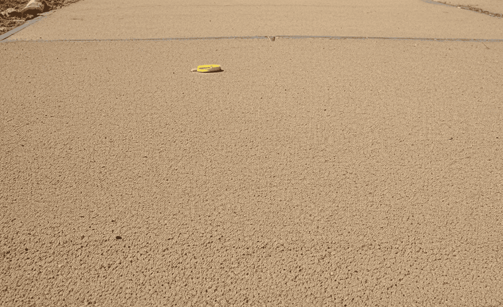 Three-quarter view of a dusty driveway work surface with chalk line reel, tape measure, marker, and notepad.