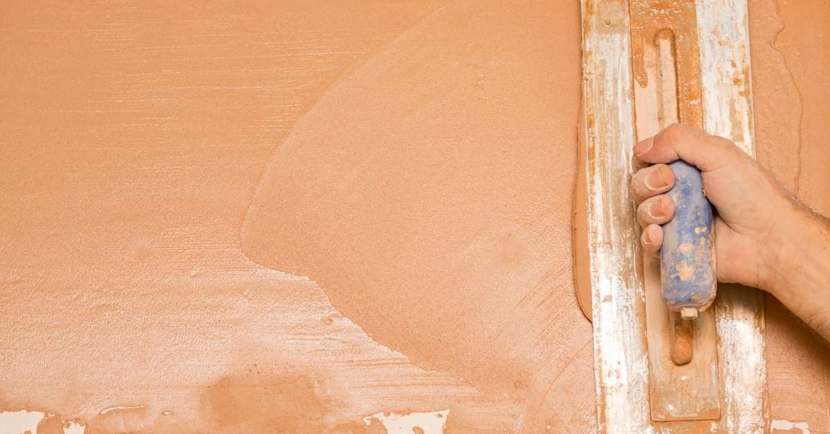 Hand using trowel to apply brown stucco coat
