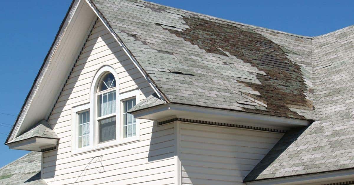Roof with cracked and missing asphalt shingles under blue sky