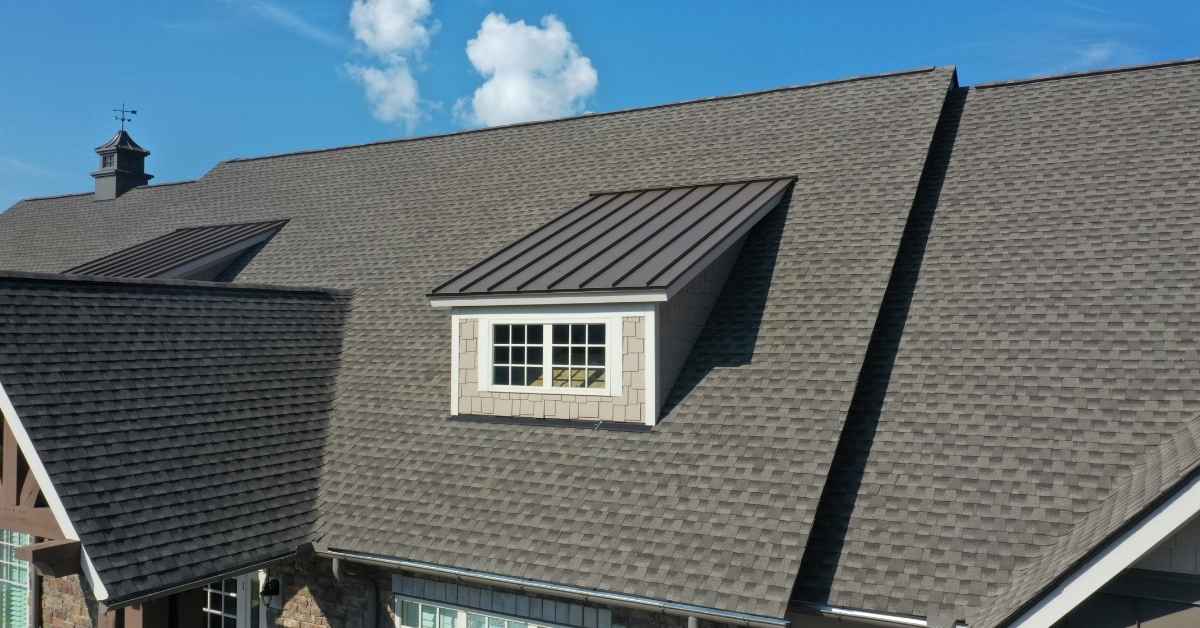 Gray asphalt shingle roof with dormer window under blue sky