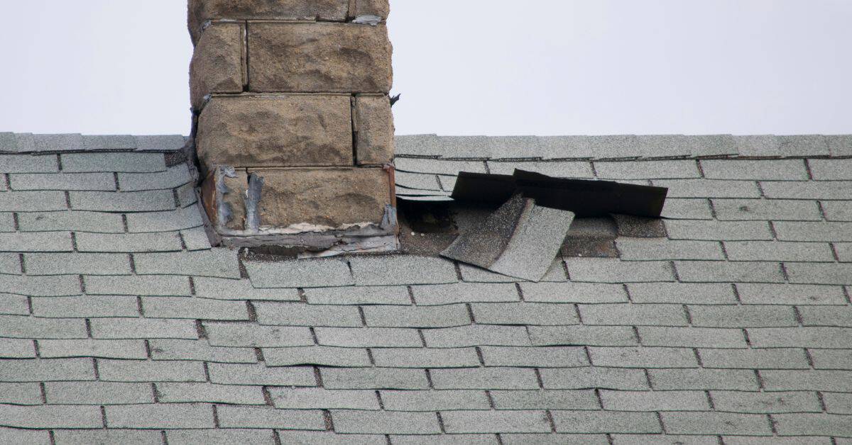 Asphalt shingles lifted near base of stone chimney