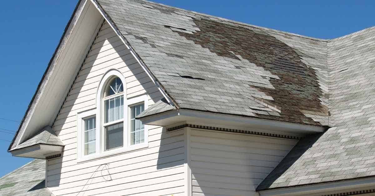 A house roof with damaged and discolored asphalt shingles