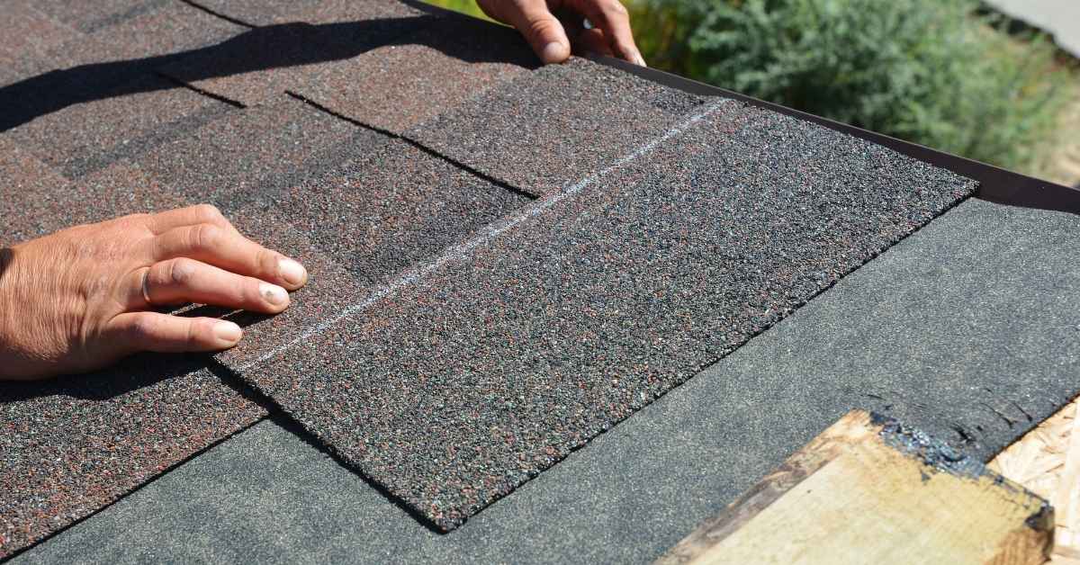 Hands installing asphalt shingles on roof underlayment