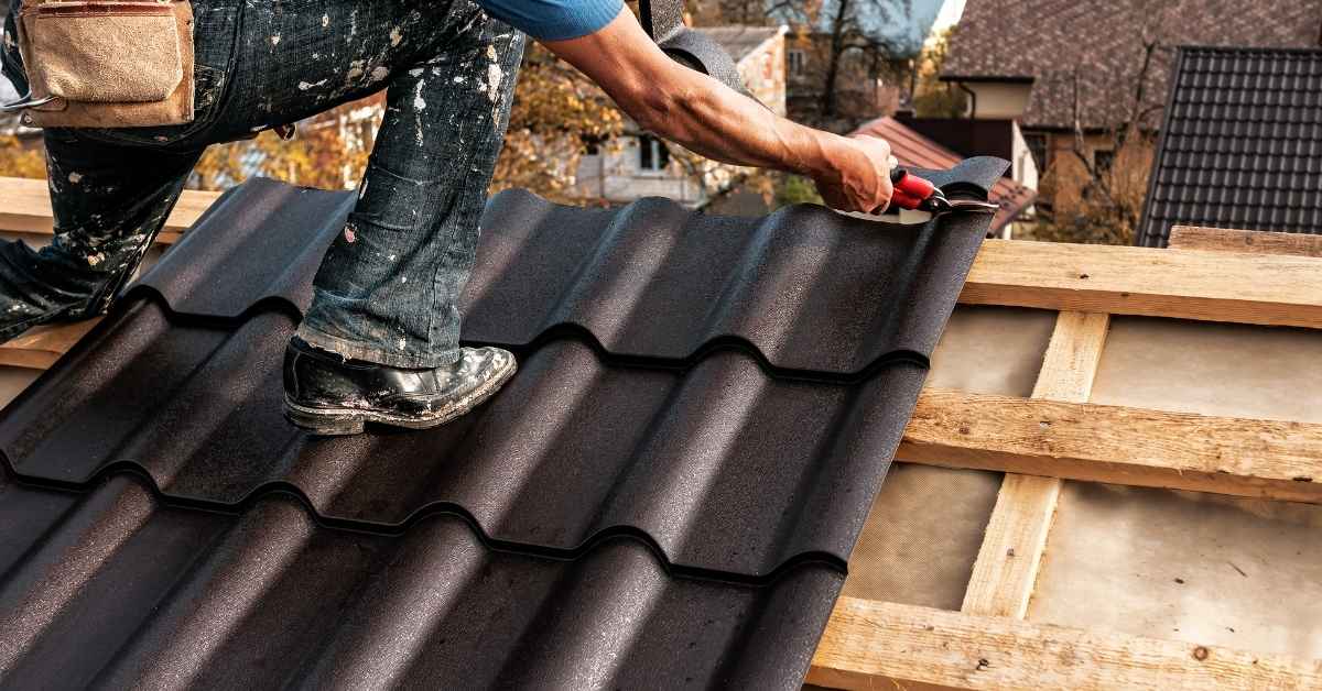 Worker installing dark brown roof panels on wooden structure