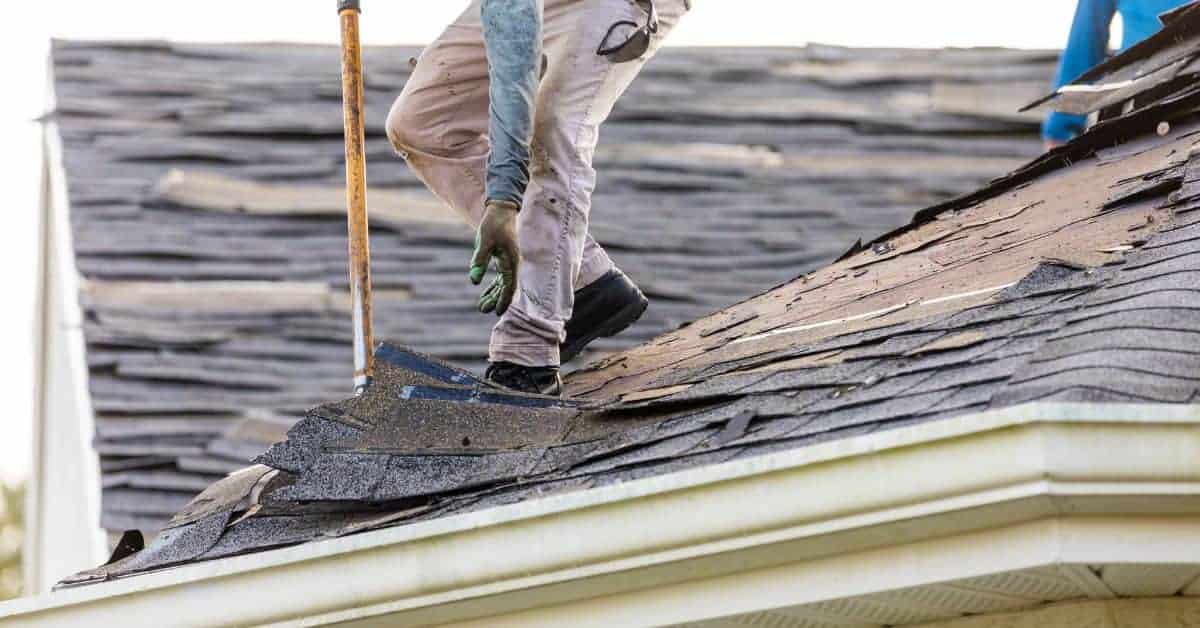 Worker removing old asphalt shingles from roof