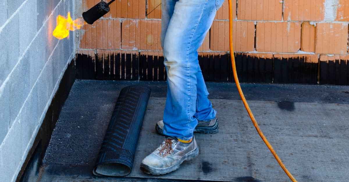 Worker using torch to install roofing membrane on flat roof