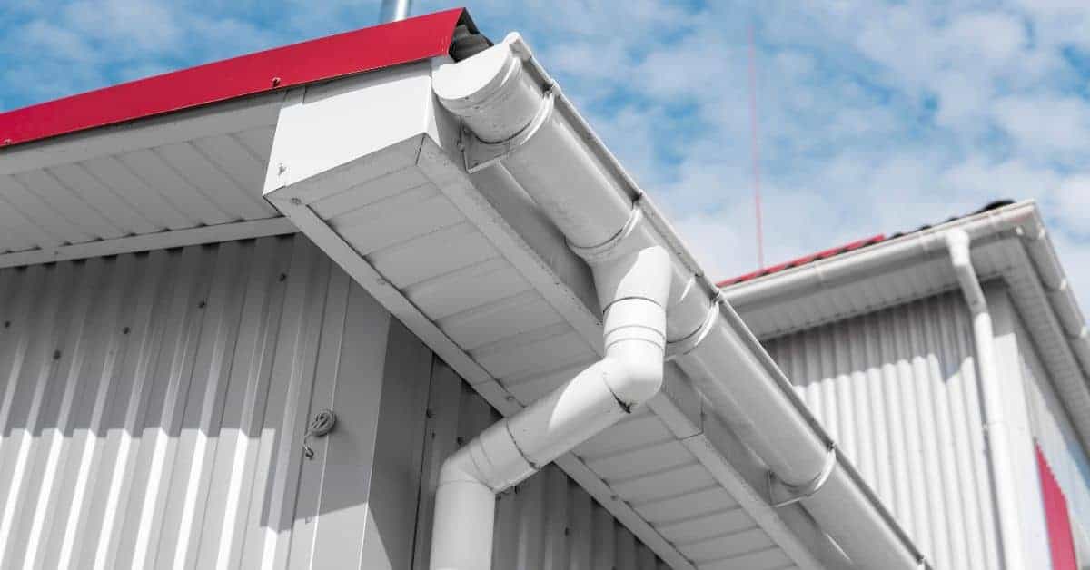 White metal gutter and downspout on building with red roof edge