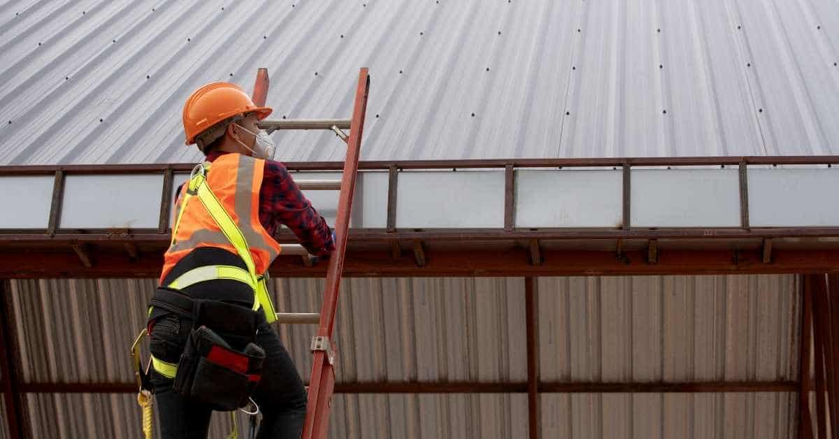 Worker in safety gear climbing ladder to metal roof