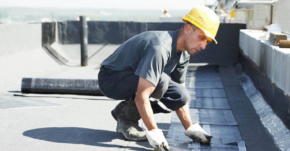Construction worker installing black roofing membrane on flat roof