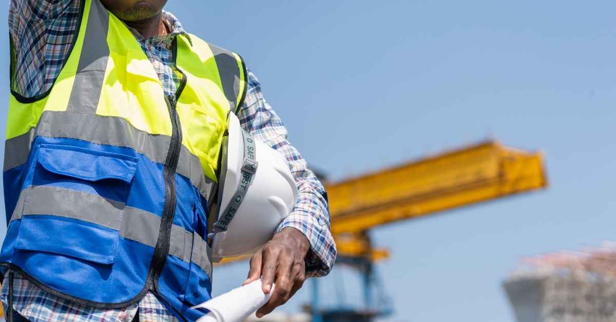 Construction worker wearing safety vest holding helmet and plans