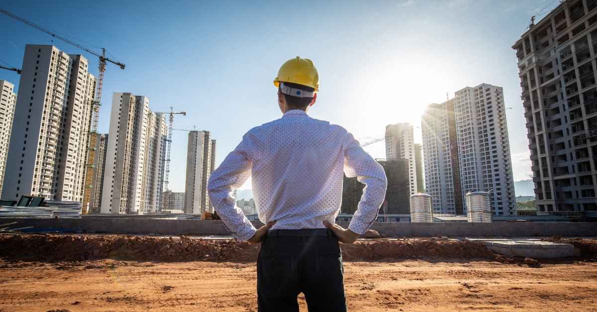 Man in hard hat overlooking construction site with buildings