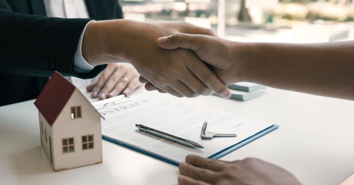 Two people shaking hands over house model and contract