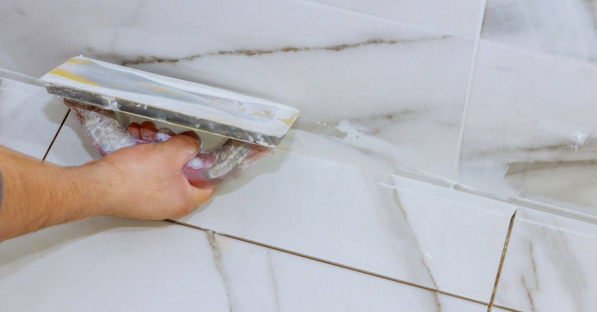 Hand using grout float on polished marble tiles