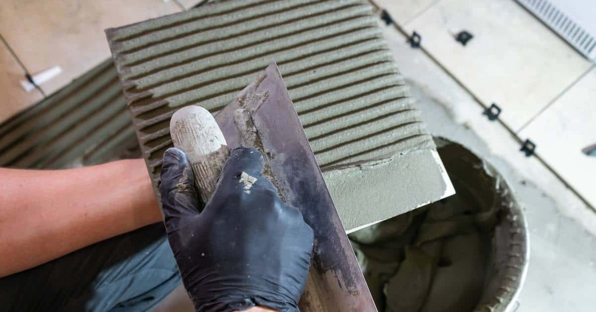 Hand spreading ridged thinset with trowel over tile surface