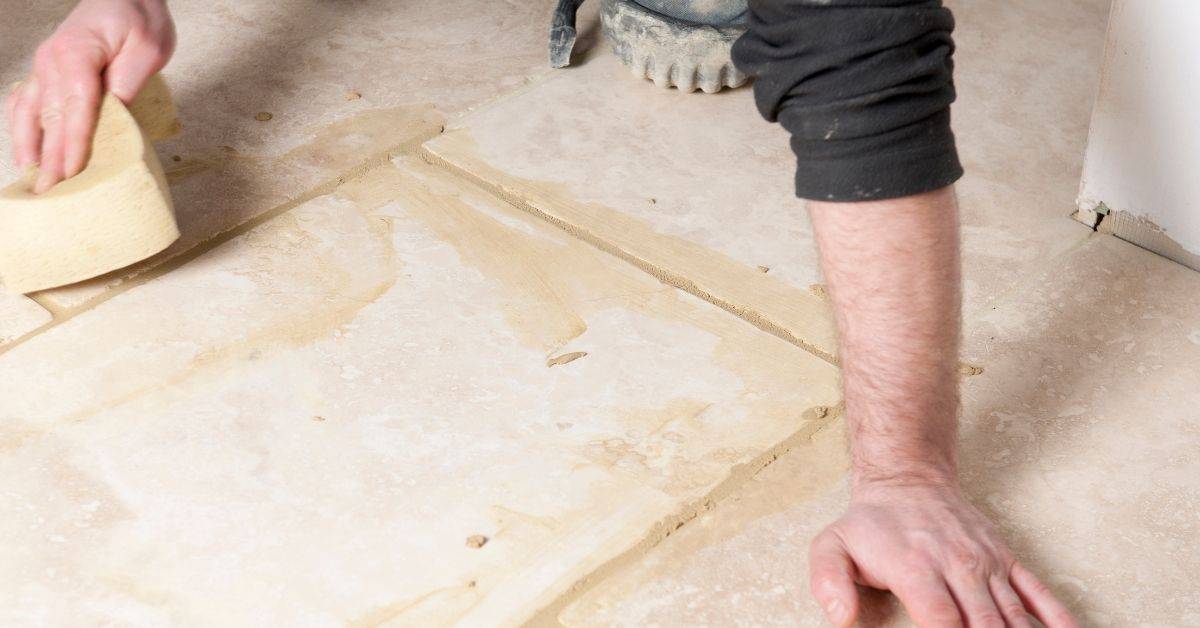 Person cleaning grout lines on tile floor with sponge