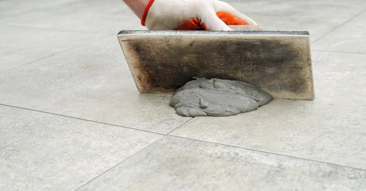 Hand spreading grout on tiled floor with grout float