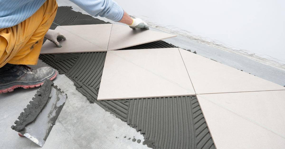 Person placing large square tiles on adhesive mortar