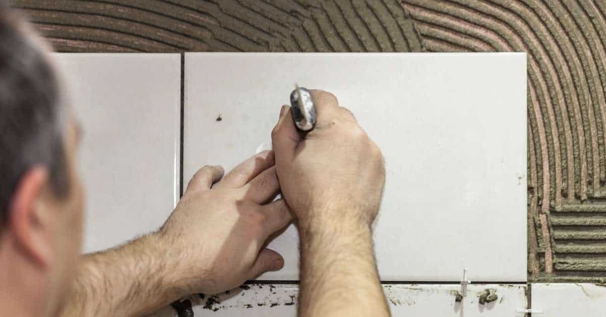 Person installing white rectangular tile with trowel and spacers