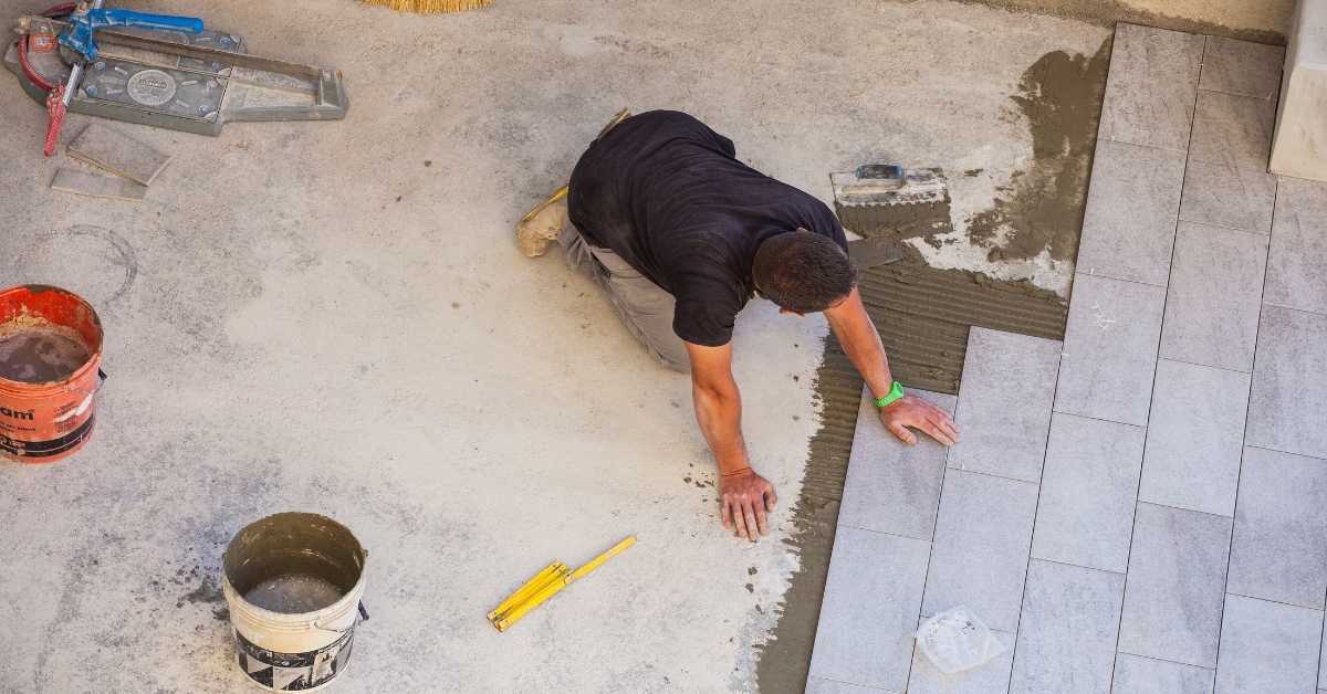 Worker installing rectangular floor tiles on concrete surface