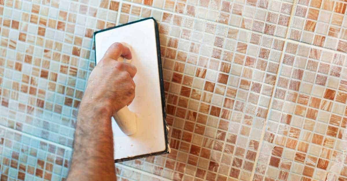 Hand holding grout float on tiled shower wall