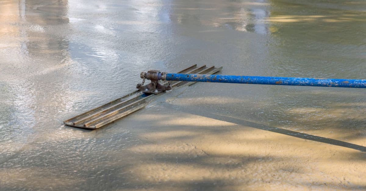 Concrete smoothing tool with long blue handle on wet concrete surface