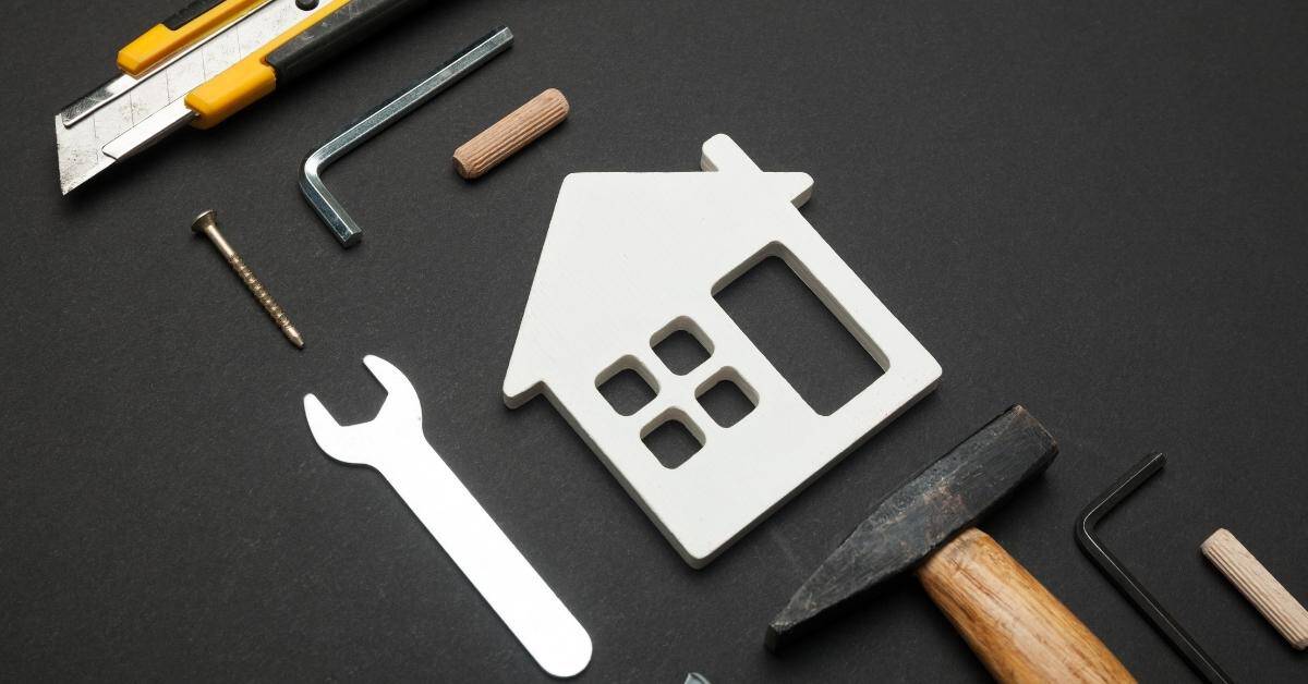 Various hand tools surrounding a white house-shaped cutout on black surface