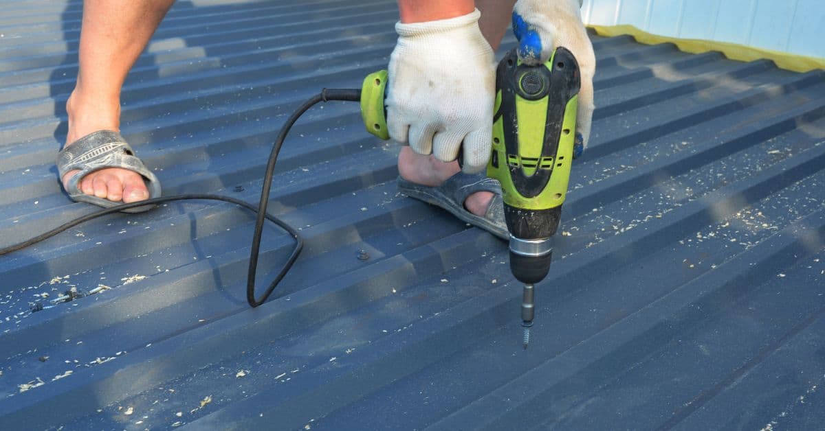 Person using electric drill on metal roof wearing gloves and sandals