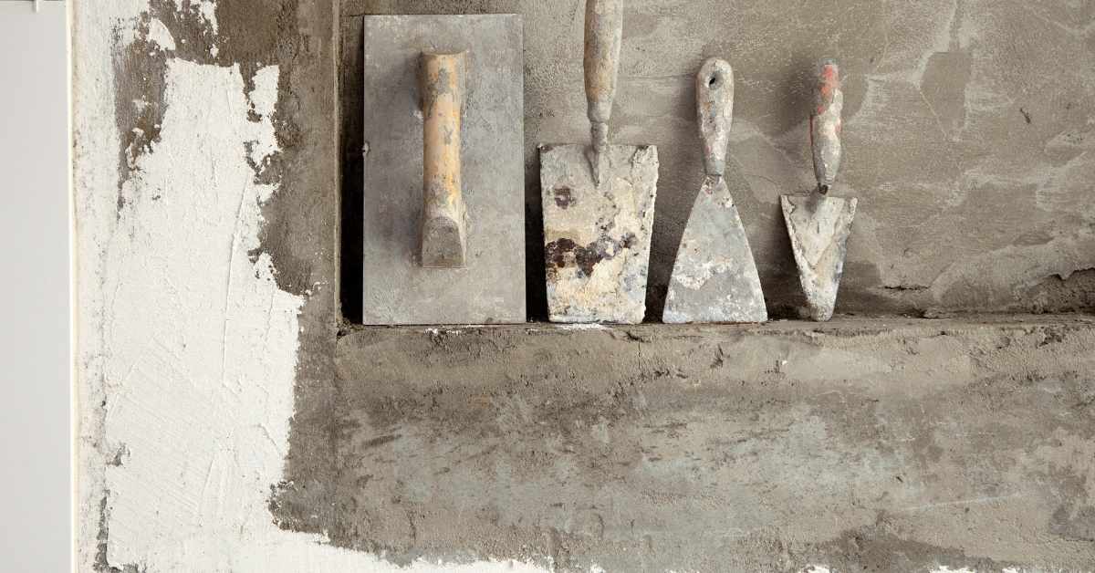 Four plastering tools hanging on partially plastered wall