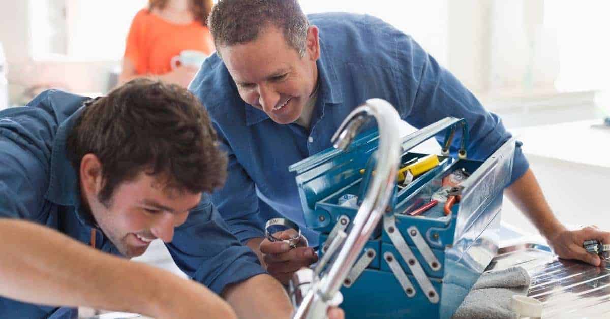 Two men working with a blue toolbox full of tools