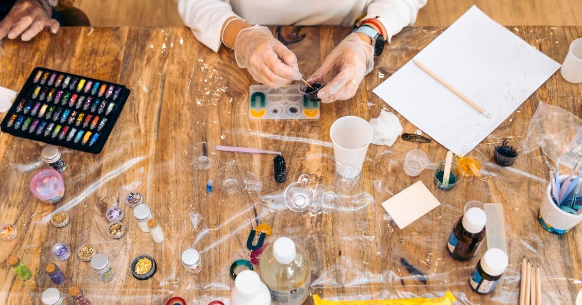 hands wearing gloves working with resin and colorful craft supplies on table