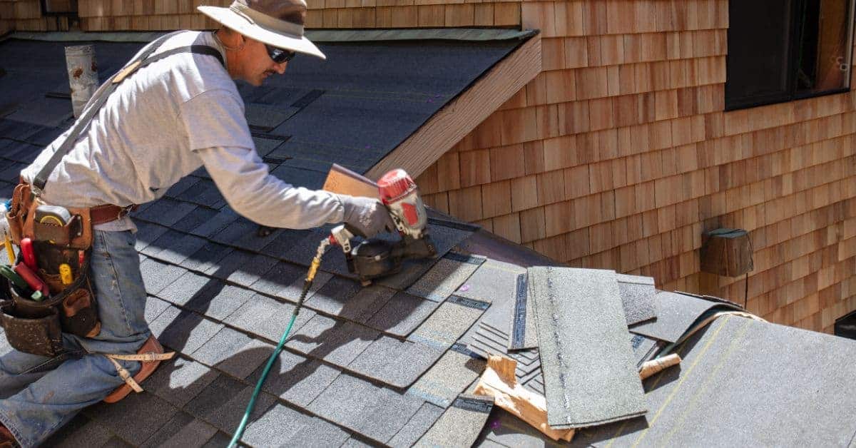 Worker installing roof shingles using nail gun and toolbelt