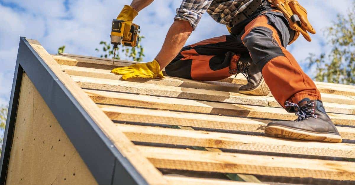 Person installing wooden sheathing on roof wearing gloves and tool belt