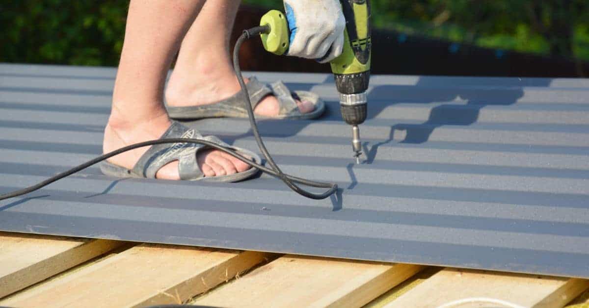 Person using electric drill on metal roof sheet wearing sandals