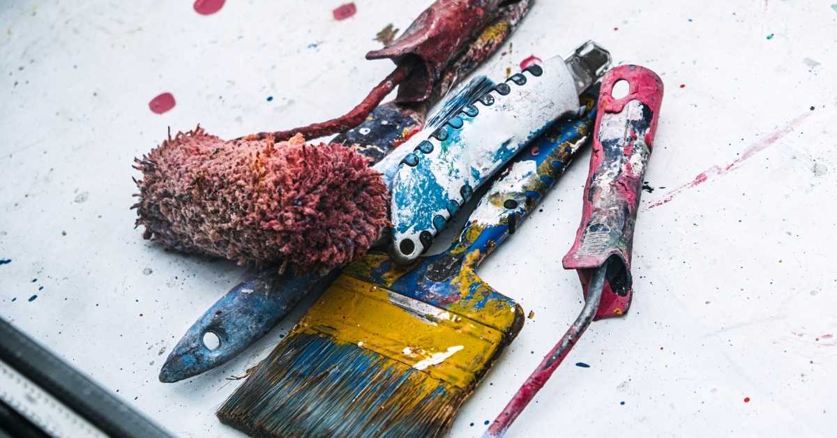 Used paintbrushes and a roller on a white surface