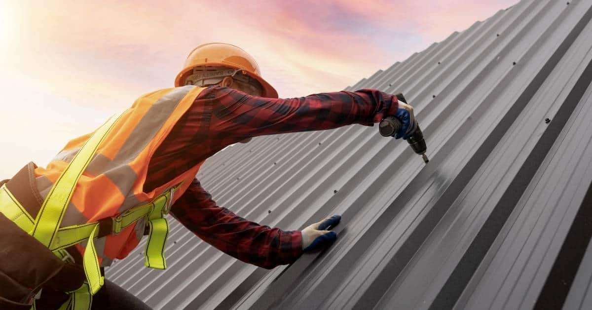 Worker in safety gear drilling screws into metal roof