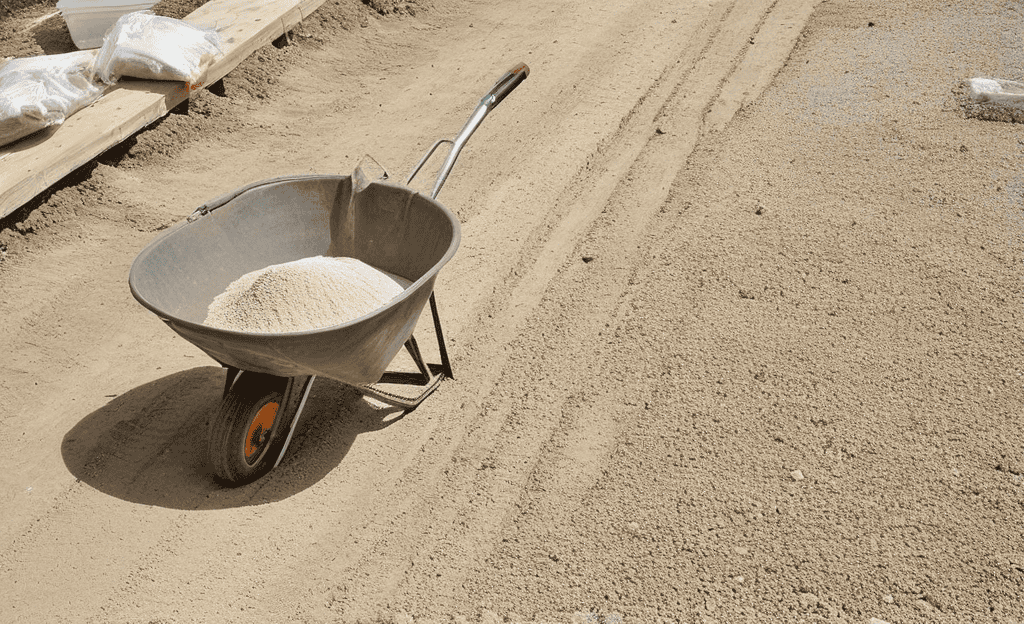 Sunlit backyard patio with cement bags, mixer, wheelbarrow, gravel, hose, formwork, rebar, PPE, and trowel.