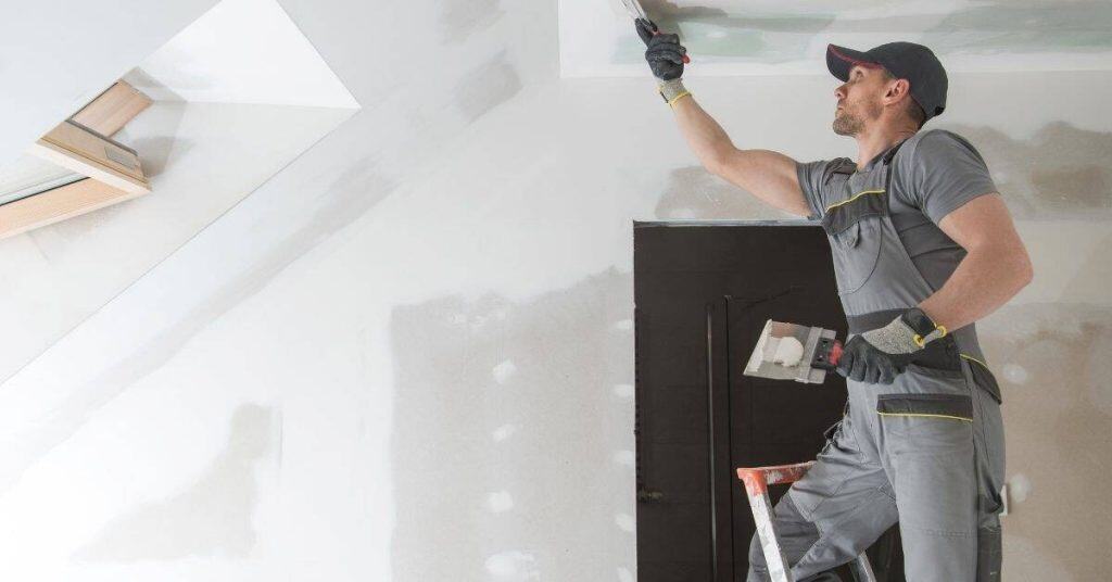 Worker applying plaster patch on ceiling using putty knife
