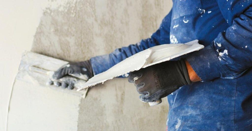 Worker applying plaster to wall with trowel and hawk