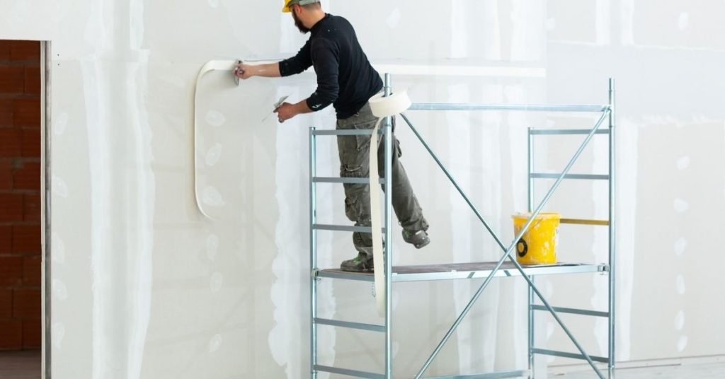 Worker applying tape to drywall seams on scaffold