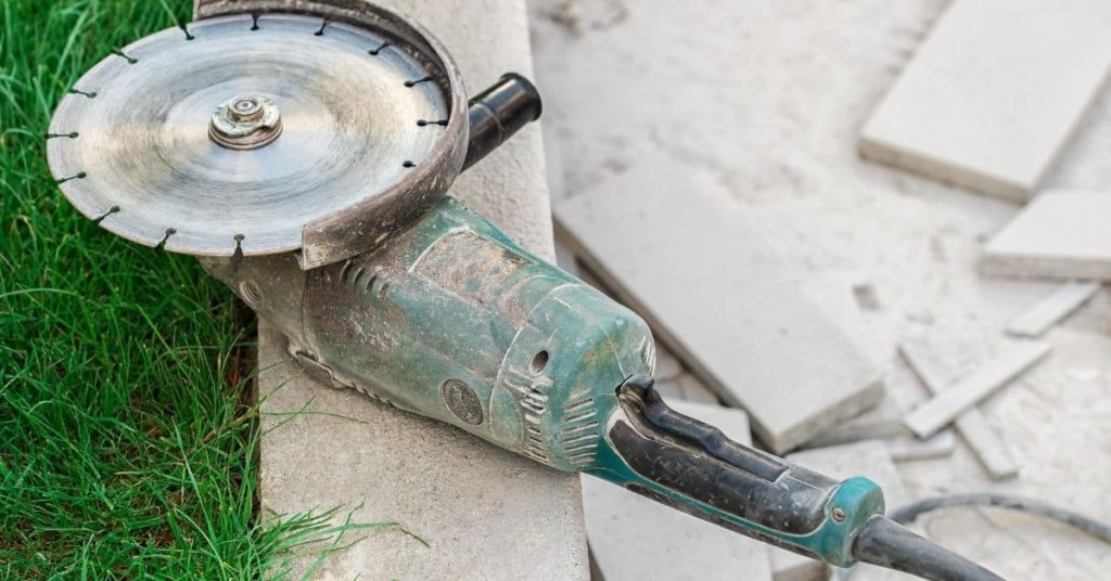 Angle grinder resting on concrete edge with cut concrete pieces