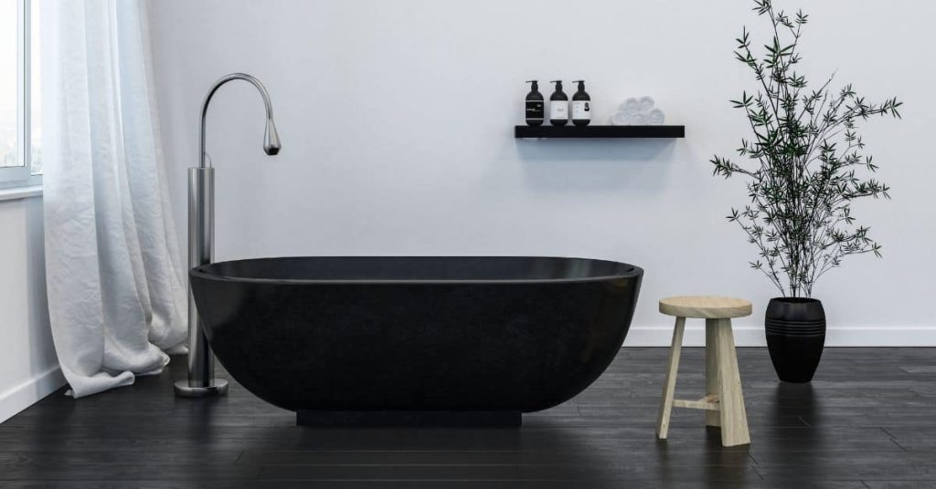 Black freestanding bathtub on dark floor with stool and plant