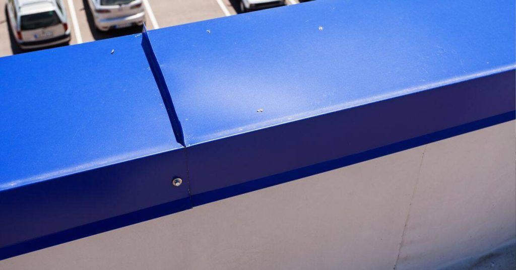 Blue metal coping joint on white concrete wall outdoors